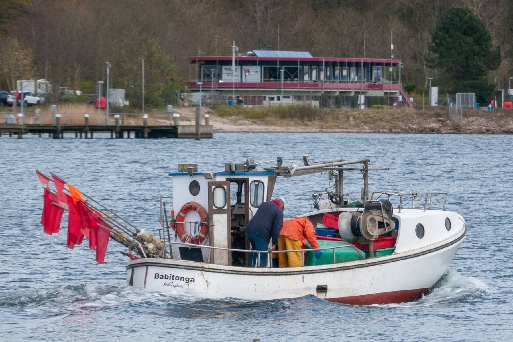 Pequena embarcação de pesca a navegar, com o pescador a trabalhar no convés